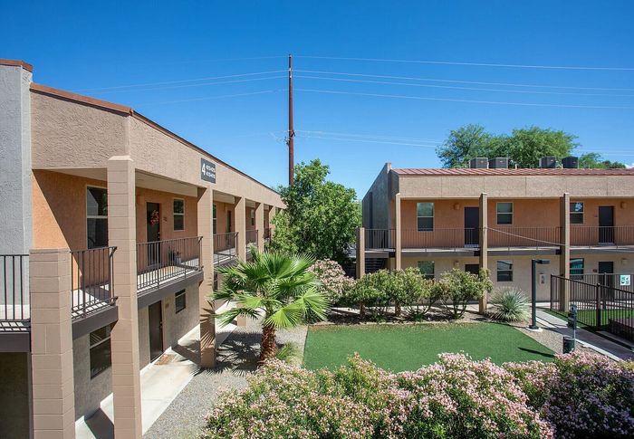 Charming apartment complex with modern balconies overlooking lush green courtyard and vibrant garden, set against a clear blue sky.