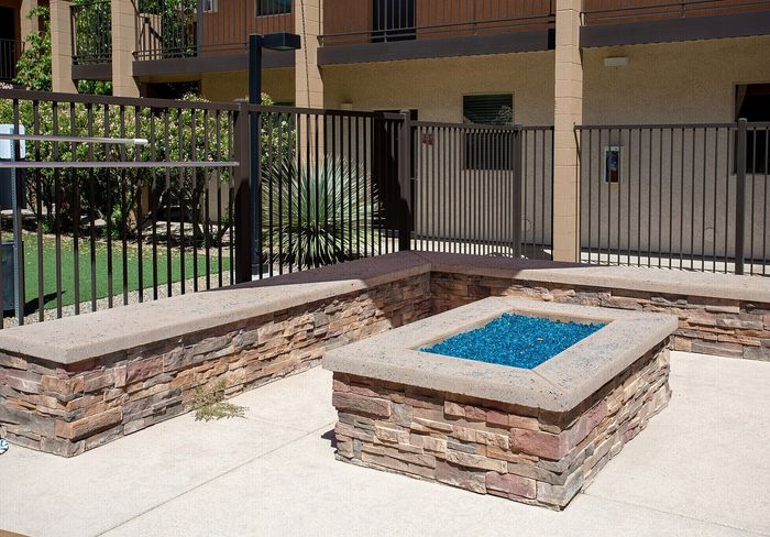 Inviting outdoor patio with modern stone seating and vibrant blue glass fire pit in a stylish apartment complex.