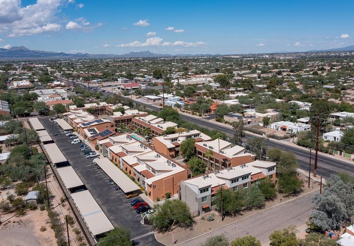 Aerial view of a modern apartment complex with solar panels, nestled in a vibrant neighborhood, under a clear blue sky with mountain views in the distance.