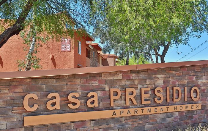 Welcoming entrance to Casa Presidio Apartment Homes with rustic stone signage and lush greenery.