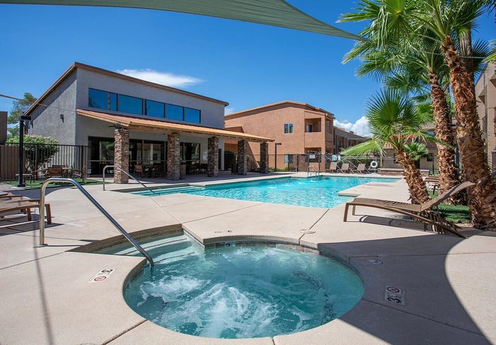 Luxurious apartment complex featuring a sparkling pool, rejuvenating hot tub, and inviting sun loungers amid lush palm trees.