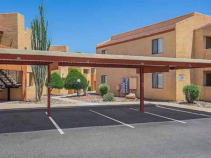 Modern apartment exterior with covered parking, surrounded by lush greenery and a peaceful environment.
