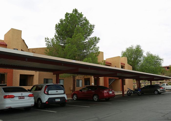 Modern apartment exterior with covered parking, surrounded by lush greenery and a peaceful environment.