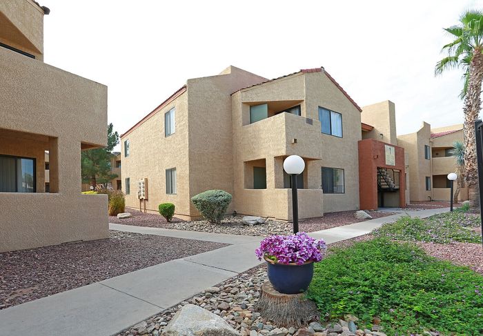 Charming apartment complex exterior with stucco finish, beautifully landscaped pathways, and vibrant flowering plants.