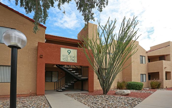 Charming desert-style apartment building with modern facade, natural landscaping, and welcoming entryway under a bright blue sky.