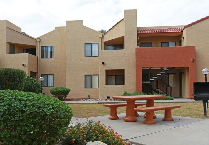 Charming apartment exterior with earthy tones, featuring a welcoming patio area, lush landscaping, and outdoor seating.