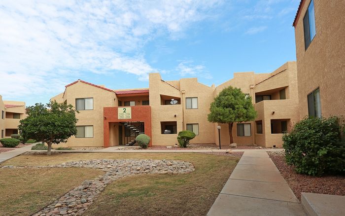 Charming apartment complex with warm stucco exteriors, lush greenery, and a peaceful courtyard setting under a vibrant blue sky.