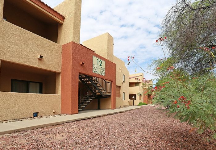 Charming desert-style apartment complex with rustic stucco exterior and inviting outdoor stairway, surrounded by lush desert greenery.