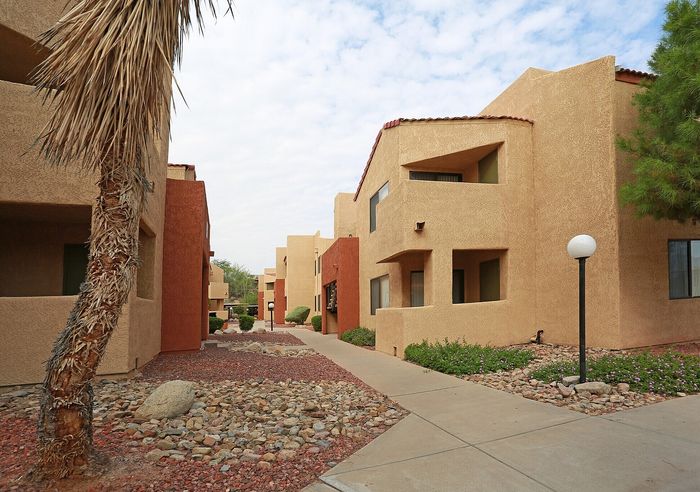Charming desert-style apartment complex showcasing warm earth-toned buildings with modern architecture, surrounded by beautifully landscaped paths and native desert plants.