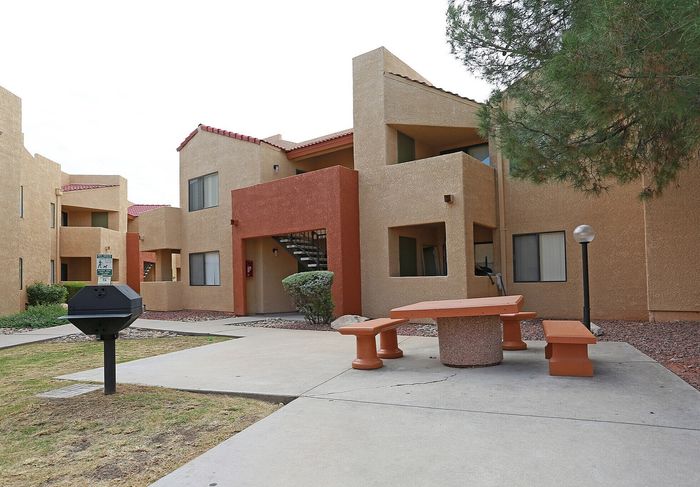 Charming apartment complex with modern architecture, featuring a communal picnic area under shady trees and a built-in BBQ grill for outdoor enjoyment.