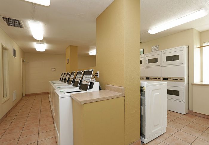 Bright and inviting laundry room equipped with modern washing machines and dryers, set in a spacious tiled area with natural lighting.
