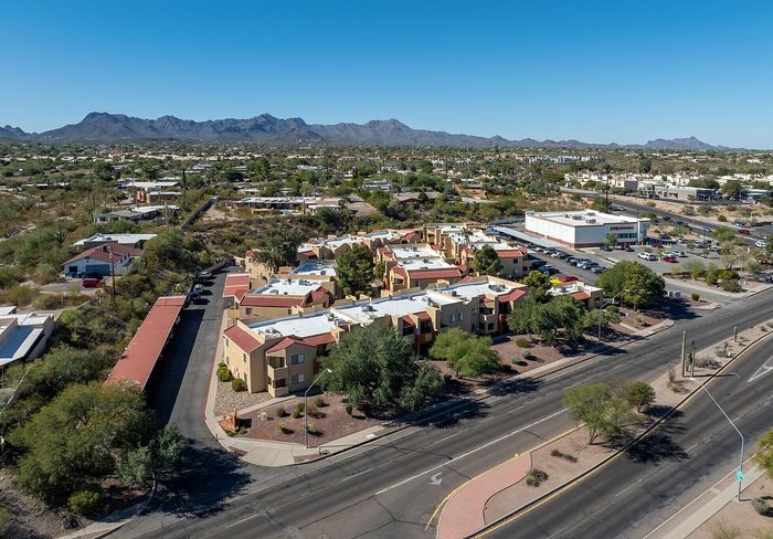 Aerial view of charming apartment complex surrounded by picturesque desert landscape and mountains, offering convenient access to nearby amenities.