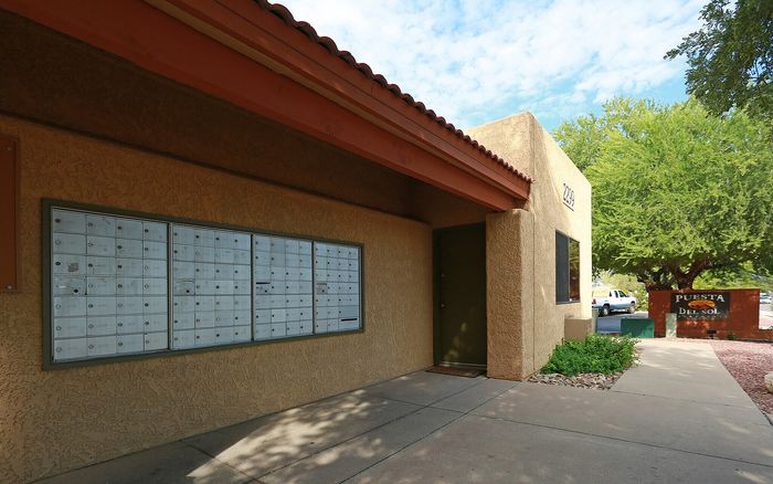 Charming apartment complex entrance showcasing a welcoming pathway, modern mailboxes, and lush greenery under a clear blue sky.