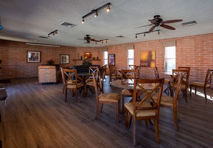 Inviting community room featuring modern track lighting, elegant wooden furniture, and a cozy brick accent wall, ideal for gatherings and social events.