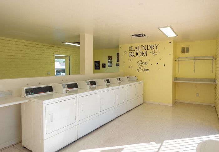 Bright and inviting laundry room with multiple modern washers, cheerful yellow walls, and playful wall art labeled 'Loads of Fun.'
