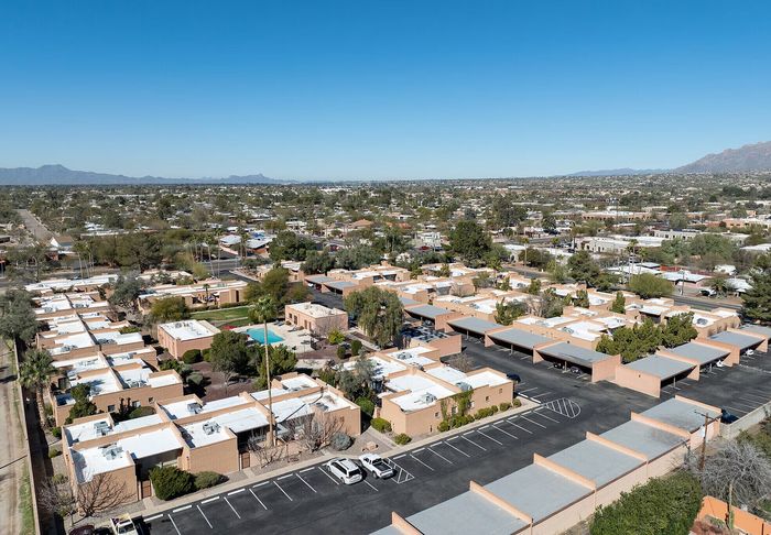 Elevated view of a charming residential community featuring modern townhomes, lush greenery, a sparkling swimming pool, and spacious parking facilities against a backdrop of scenic mountains.