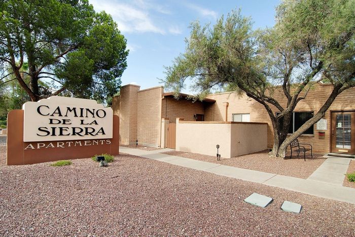 Charming Camino De La Sierra Apartments entrance with lush green trees and inviting pathways.
