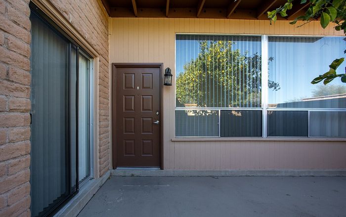Charming apartment entrance with brick and wood exterior, featuring a large window reflecting lush greenery.