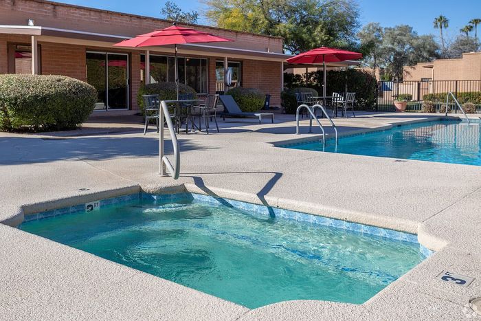 Inviting outdoor pool area featuring a sparkling swimming pool and cozy hot tub with stylish red umbrellas and lush greenery.