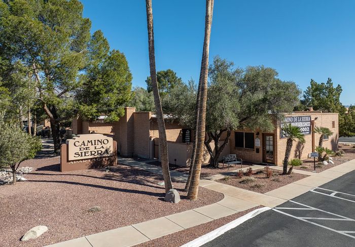 Charming Camino De La Sierra Apartments with inviting pathways and lush greenery, offering a tranquil residential environment under a clear blue sky.