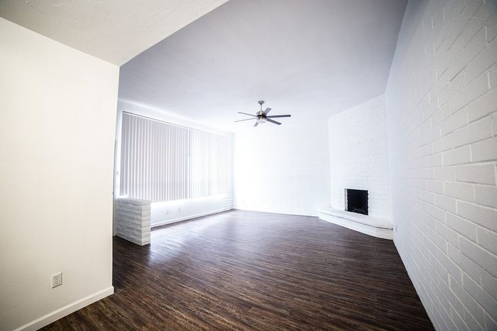 Bright, spacious living room with elegant wood flooring, floor-to-ceiling windows, and a stylish ceiling fan.