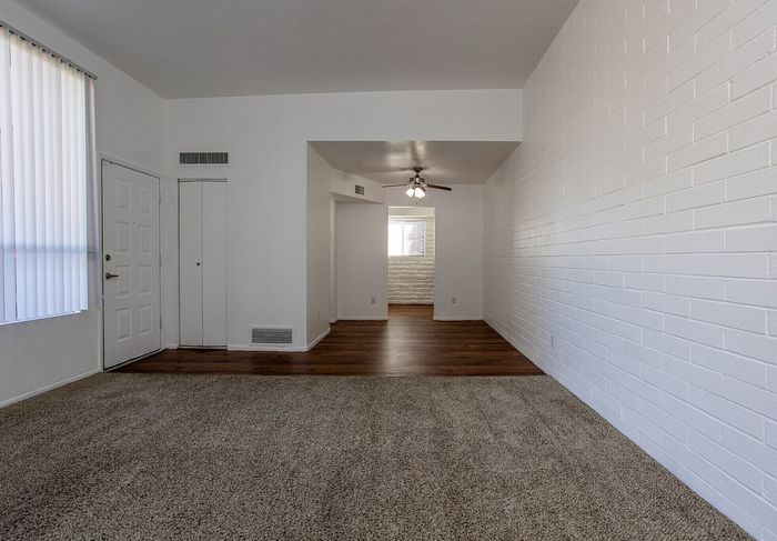 Inviting living room with a mix of plush carpet and sleek hardwood flooring, accented by a stylish ceiling fan and expansive white brick accent wall.