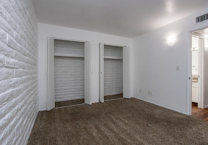 Chic apartment bedroom with textured white brick wall, dual closets, and plush carpet flooring.