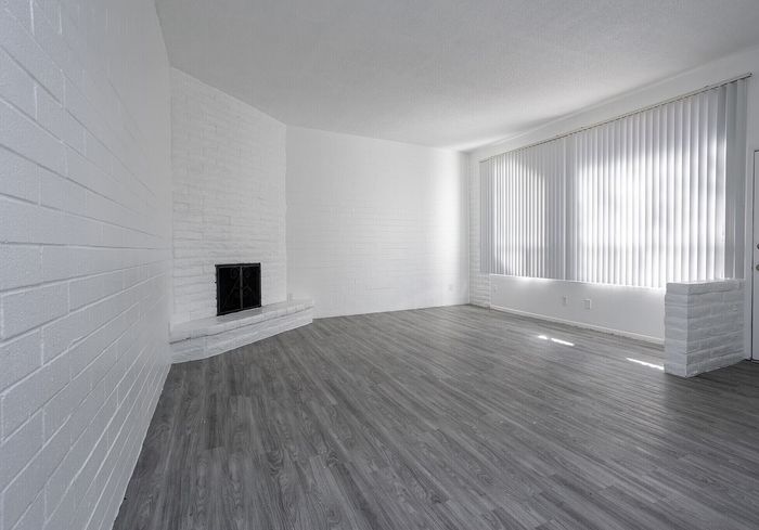 Spacious and elegant living room with modern gray laminate flooring, bright natural light, and a charming white brick fireplace.