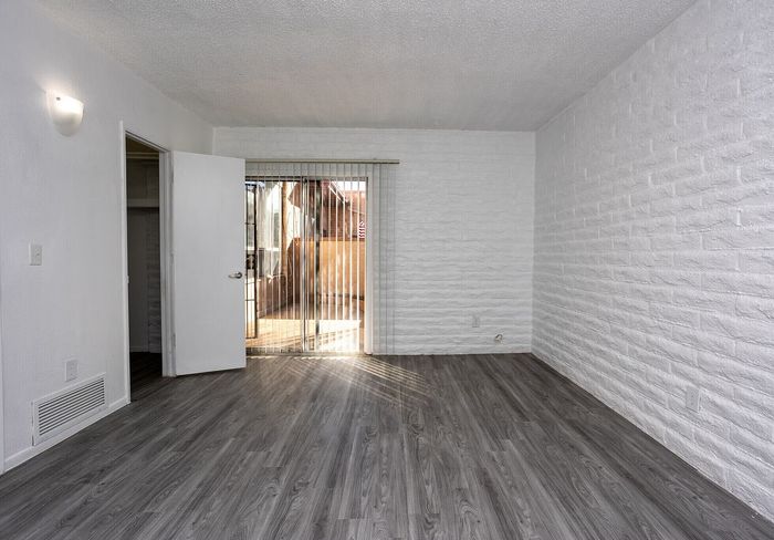 Bright and inviting room with elegant wood flooring, white brick walls, and a door leading to an outdoor patio.