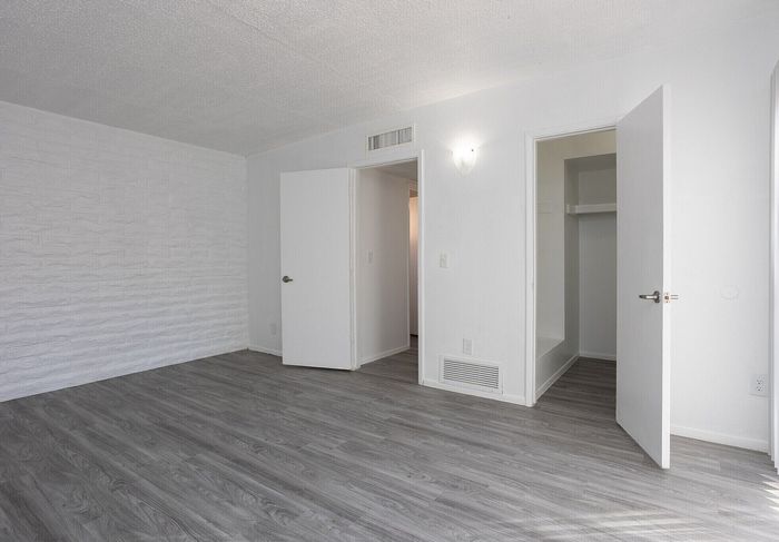 Bright and inviting room featuring elegant gray flooring, textured white walls, ample closet space, and modern lighting.