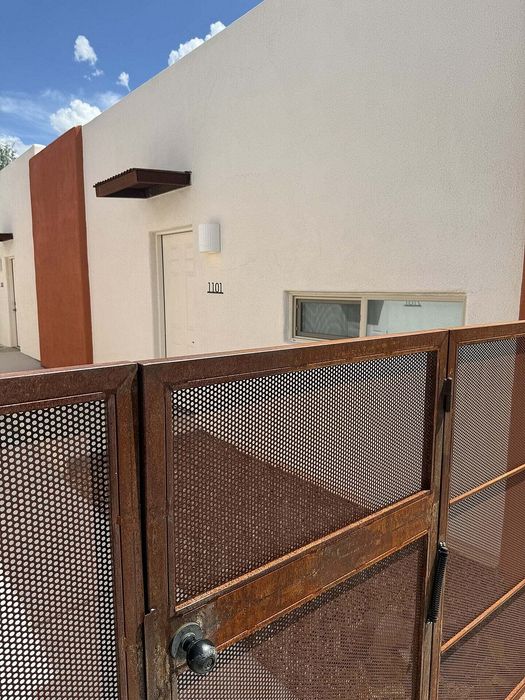 Charming modern apartment entrance with a stylish perforated metal gate and clean architectural design under a sunny sky.