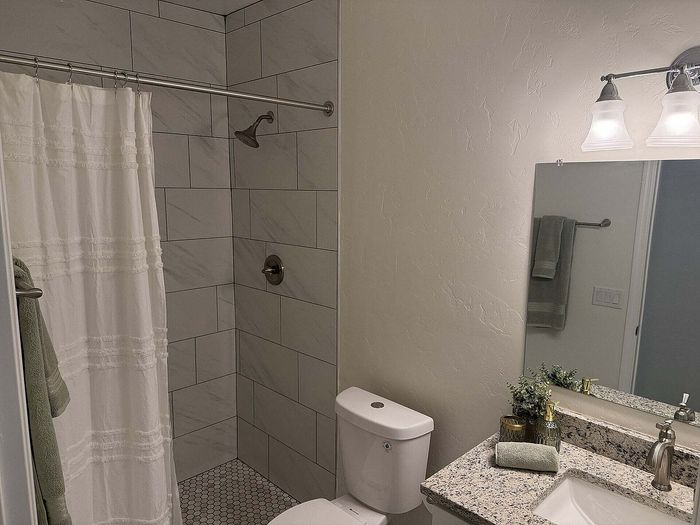 Elegant bathroom featuring a modern tiled shower, granite countertop, and soft ambient lighting.