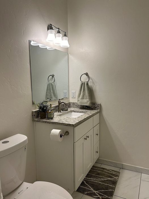 Elegant bathroom with modern fixtures, featuring a granite countertop, stylish lighting, and a sleek white vanity.