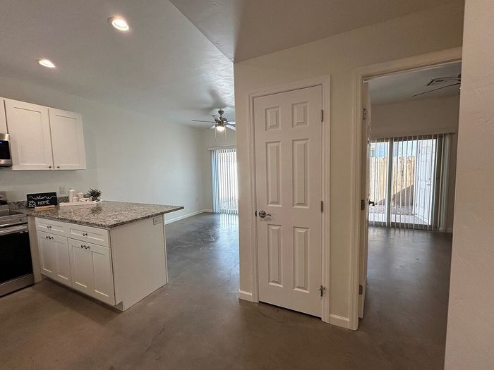 Modern apartment with open kitchen featuring granite countertops, sleek white cabinetry, and a sunlit living area with large sliding doors.