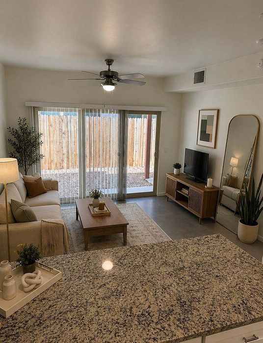 Inviting living room with modern decor, featuring a cozy sofa, sleek media stand with TV, and large sliding glass doors opening to a private outdoor space. The room is accented with stylish plants and a ceiling fan for comfort.
