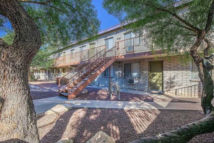 Charming apartment exterior with rustic staircase, surrounded by lush greenery and serene pathways.