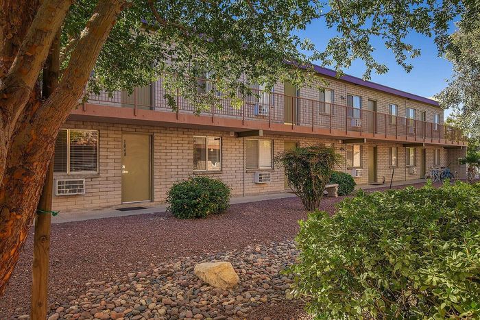 Charming two-story apartment building with lush greenery and a peaceful courtyard setting.