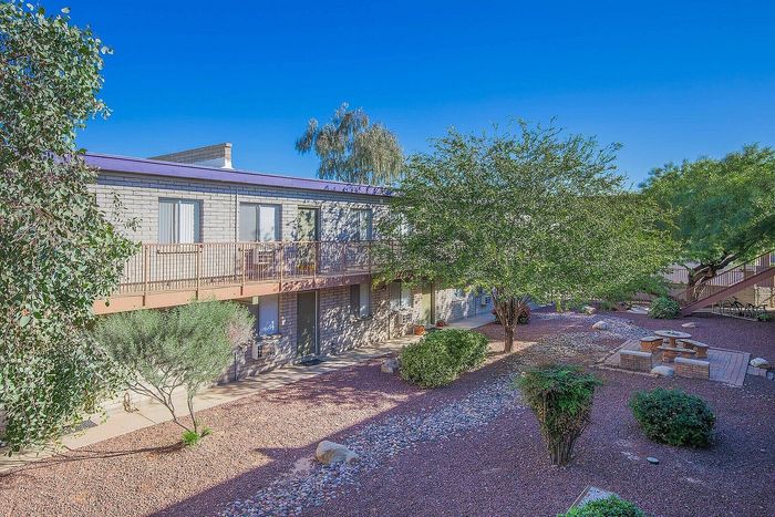 Inviting apartment exterior with a sunny courtyard, lush trees, and relaxing picnic area, perfect for a tranquil living experience.