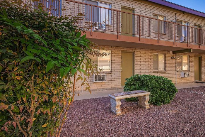 Inviting apartment exterior with lush greenery, charming brick facade, and decorative stone bench.