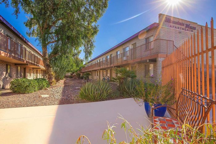 Charming apartment complex with sunlit pathways, lush greenery, and cozy outdoor seating.