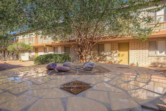 Charming apartment complex with rustic brick exterior, lush greenery, and inviting patio area featuring a decorative tile table.