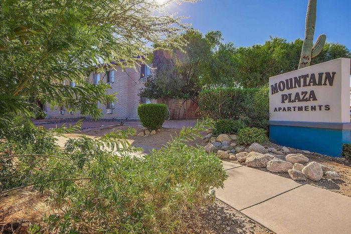 Inviting exterior of Mountain Plaza Apartments, featuring lush greenery, a well-maintained path, and a prominent sign under clear blue skies.