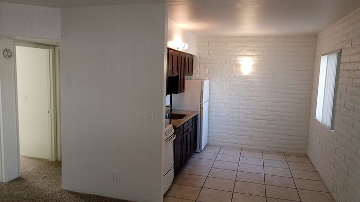 Charming apartment interior featuring a cozy kitchen with dark wood cabinets, open living space with bright white brick walls, and plush carpeted doorway.