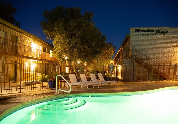 Charming Mountain Plaza Apartments at night featuring inviting poolside views with relaxing loungers and glowing lights.