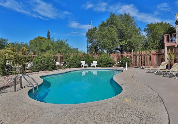 Inviting outdoor swimming pool with sun loungers, surrounded by lush greenery and a clear blue sky.