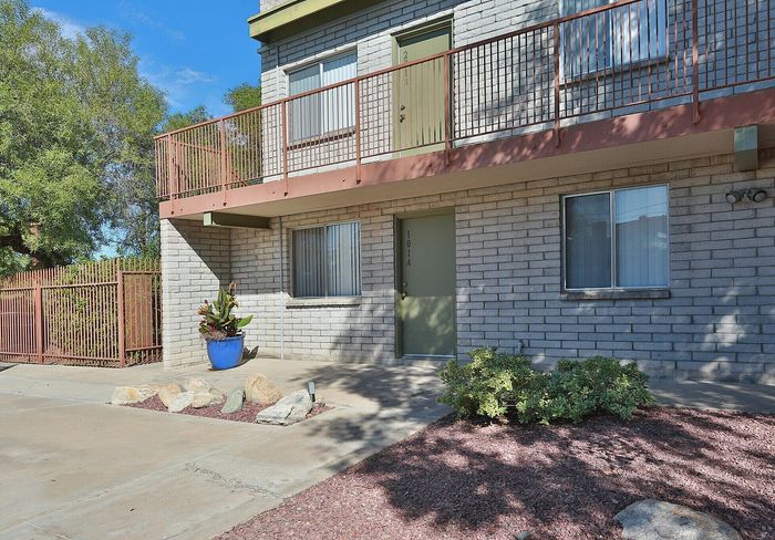 Charming apartment exterior with stylish brick facade, welcoming green door, and vibrant landscaping in desert blooms.
