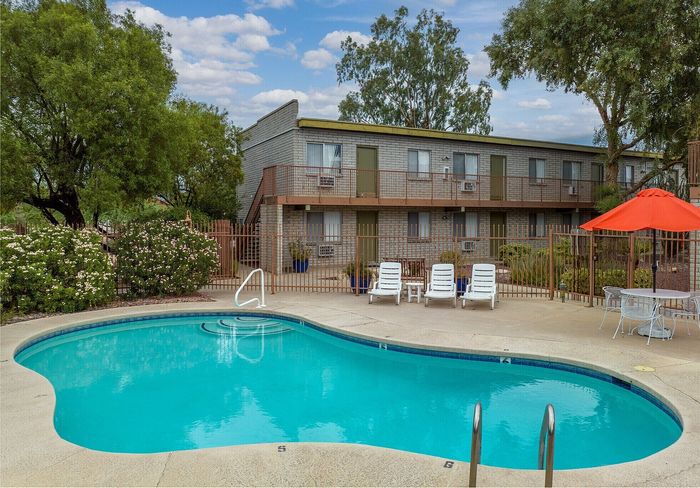 Inviting apartment complex featuring a sparkling pool, relaxing lounge chairs, and lush greenery, perfect for leisure and enjoyment.