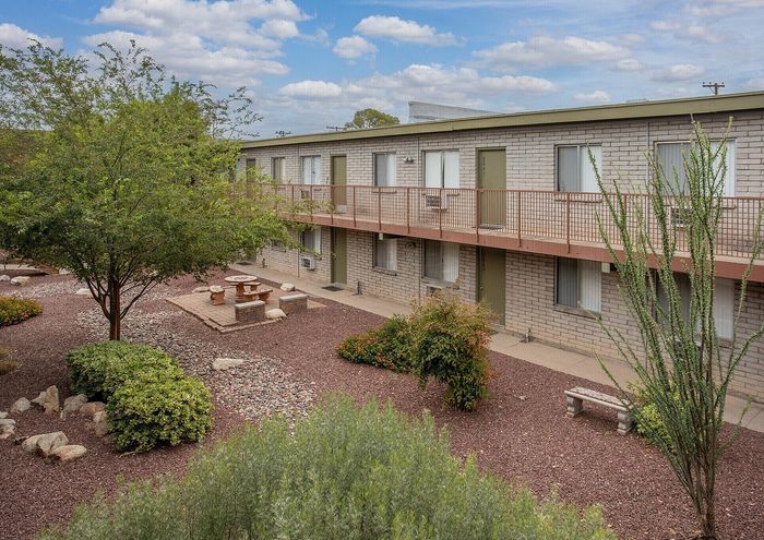 Charming courtyard view with lush greenery and a tranquil seating area, adjacent to a modern apartment building.