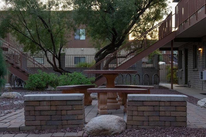 Charming courtyard with rustic brick seating and tables surrounded by lush greenery and elegant staircase.