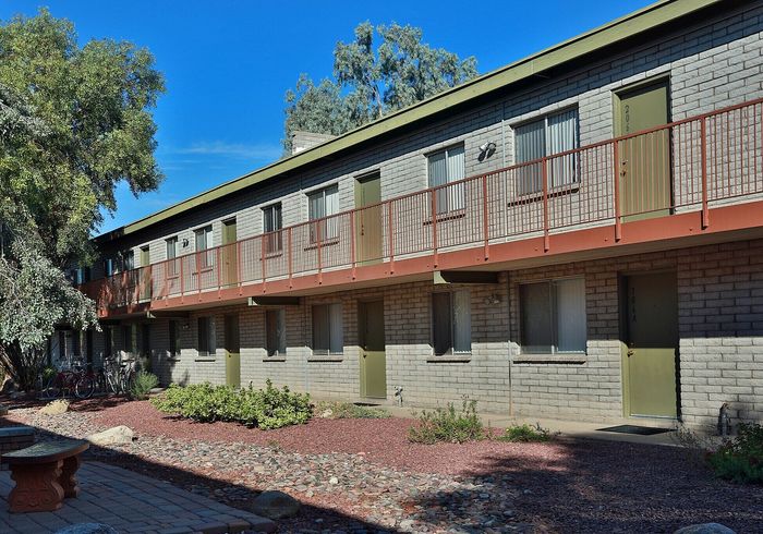 Charming apartment exterior with rustic brickwork, lush greenery, and inviting balconies under a clear blue sky.